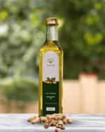 The Deep Soil Cold-Pressed Groundnut Oil 500ml glass bottle with a pile of whole peanuts on a marble surface and blurred nature background