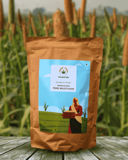 The Deep Soil Pearl Millet Flour Bajra Ka Atta package on wooden table with standing bajra crop background