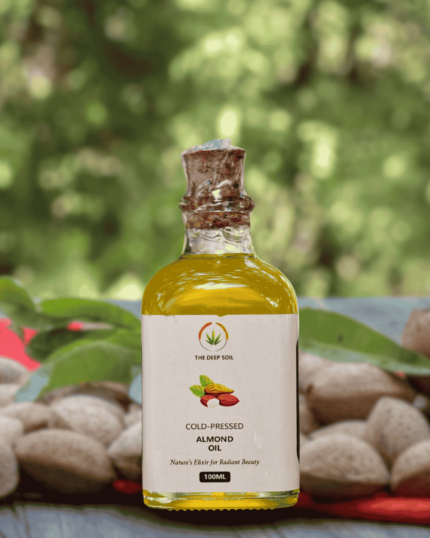 The Deep Soil Cold-Pressed Almond Oil 100ml glass bottle with a cork stopper and raw almonds in a blurred nature background