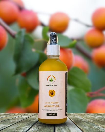 The Deep Soil Cold-Pressed Apricot Oil 100ml dropper bottle on a wooden deck with a blurred apricot orchard background