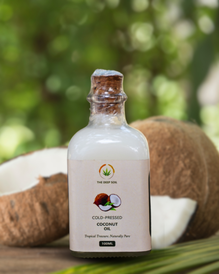 The Deep Soil Cold-Pressed Coconut Oil 100ml glass bottle with a cork stopper and fresh coconut halves in a blurred nature background