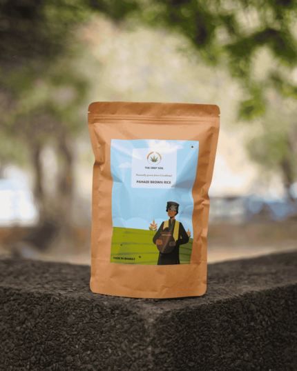 The Deep Soil Pahadi Brown Rice brown paper package on a stone surface with green park background