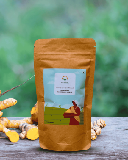 The Deep Soil Pahadi Haldi Turmeric Powder package with raw turmeric roots on a wooden surface and blurred greenery background