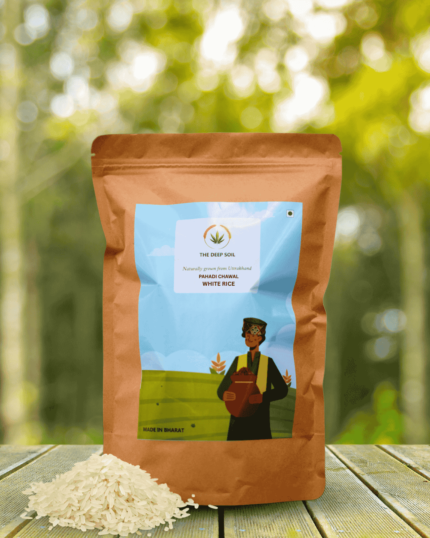 The Deep Soil White Rice Pahadi Chawal package with a small pile of loose grains on a wooden table and sunlit forest background